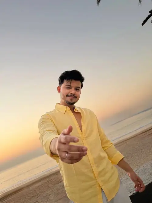 Candid Sunlit Beach Boardwalk Portrait of Playful Young South Asian Man Winking in Pastel Yellow Linen Shirt Extending H — AI Photo Editing Prompt on Faymas